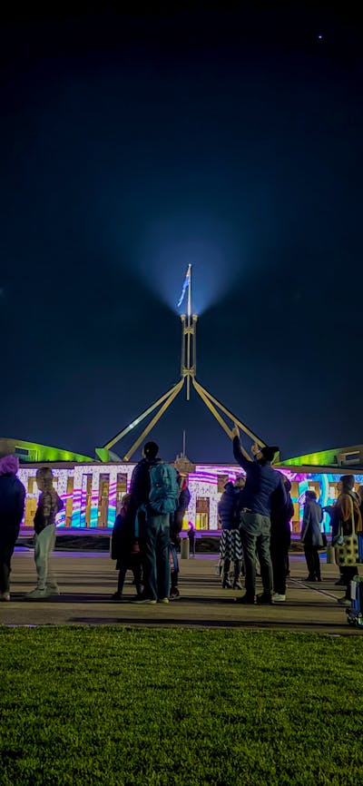Night-time view of Australian Parliament House with the illuminated flag mast rising into a dark sky
