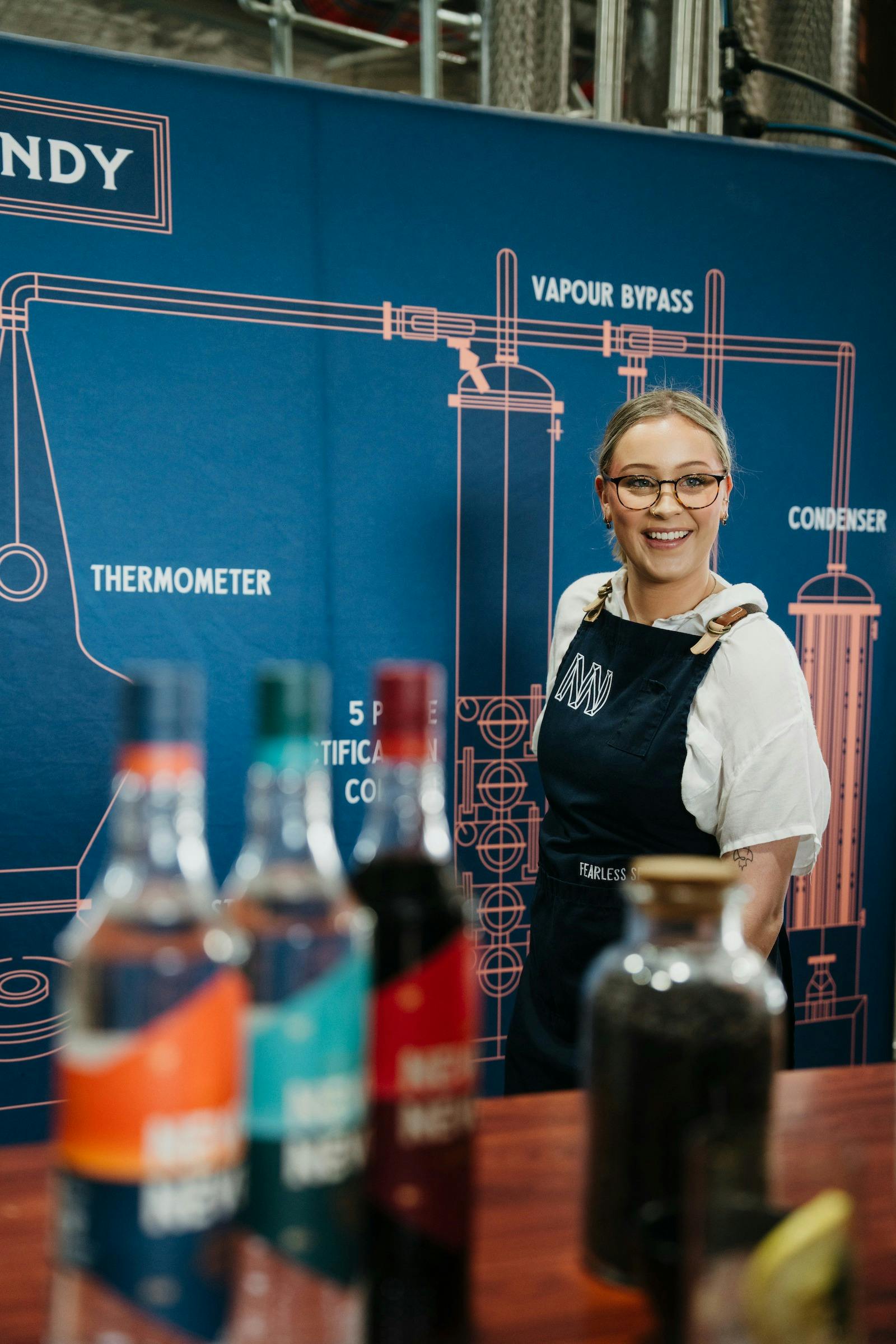 Gin expert standing infront of image of still with three bottles of gin infront