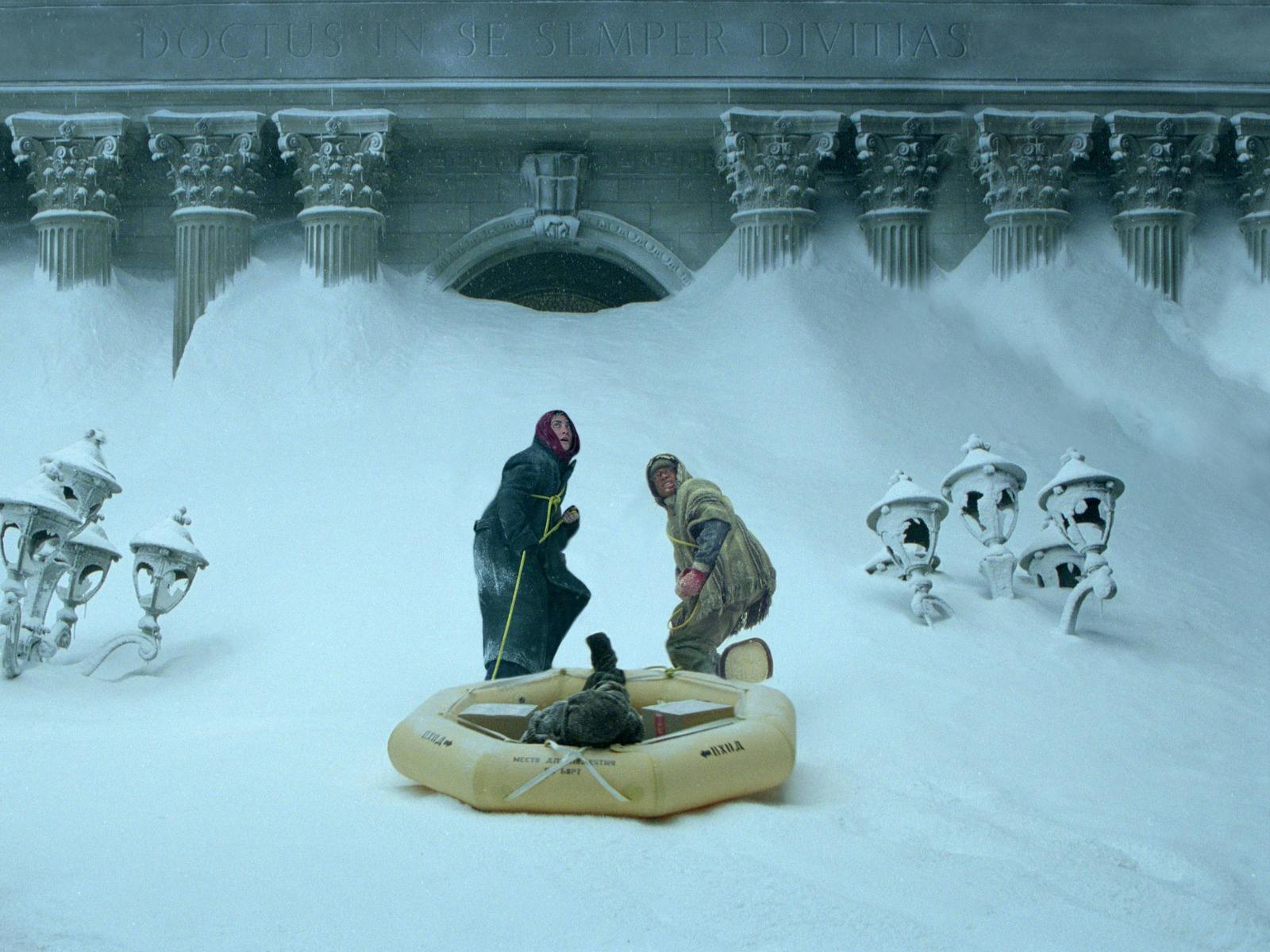 Two men in snow pulling a blow up boat looking scared and cold