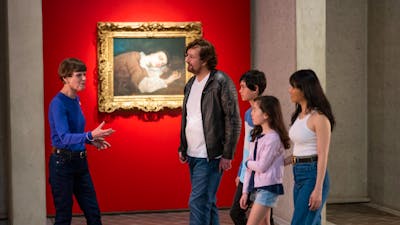A tour guide and a family in front of a framed artwork in a gallery
