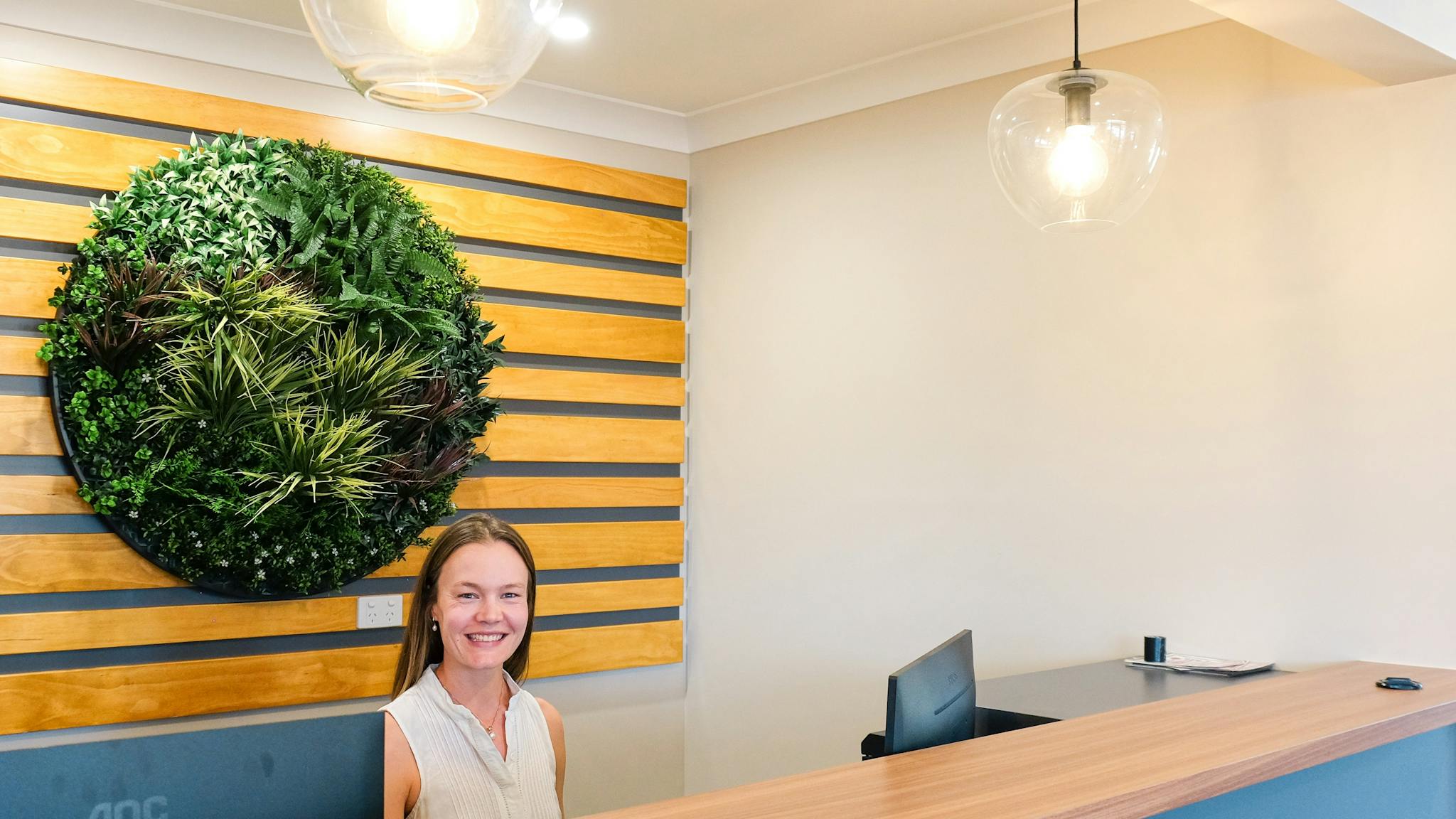 Inside reception area with a women sitting behind the desk. Green round plant in the background