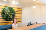 Inside reception area with a women sitting behind the desk. Green round plant in the background