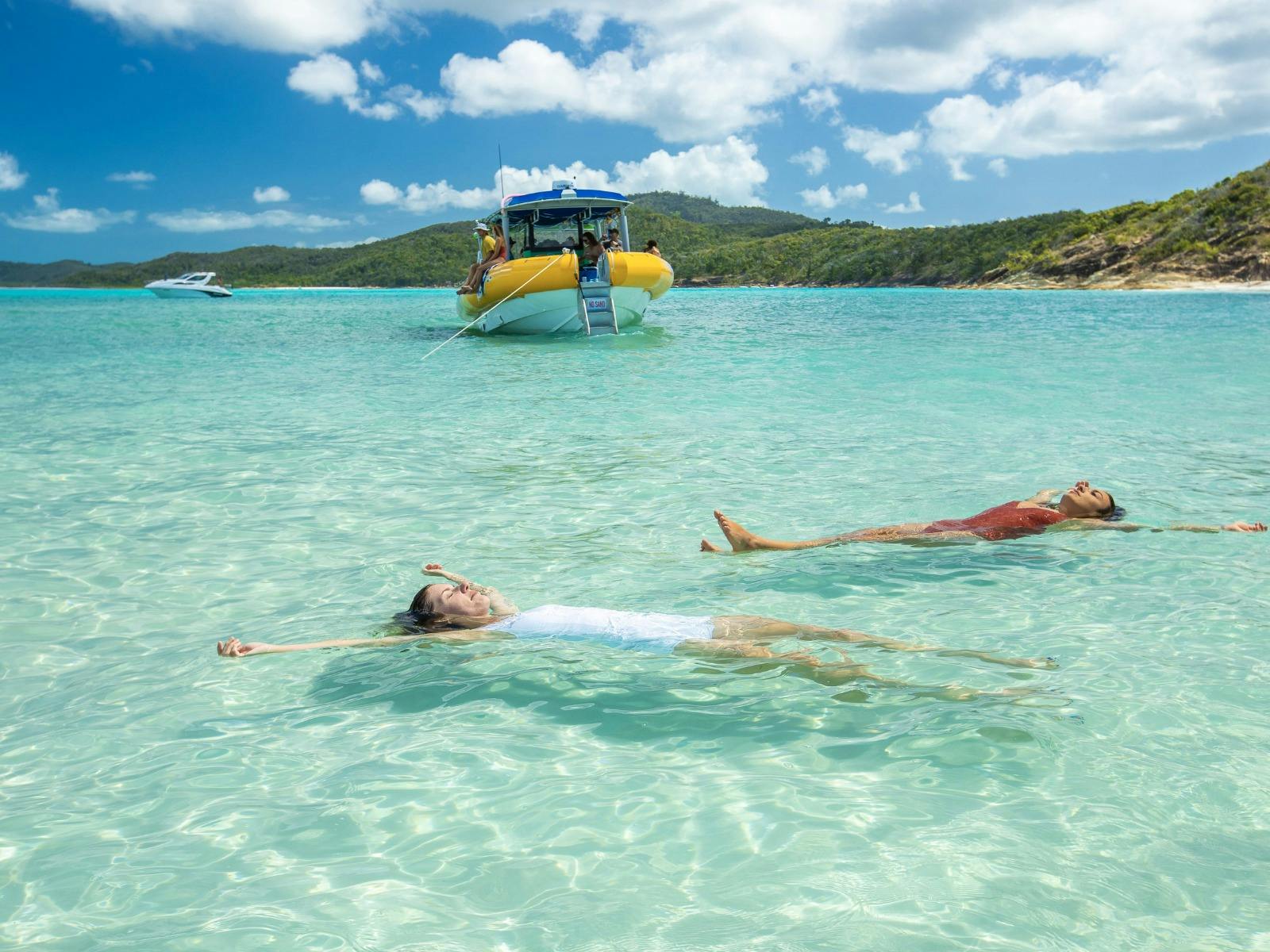 Two women floating on their backs in crystal-clear turquoise water, Whitsundays