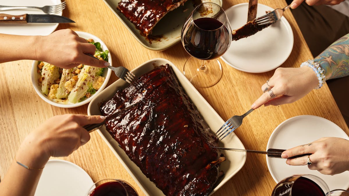Delicious racks of Hurricane's flame-grilled pork ribs being cut into with knives and forks.