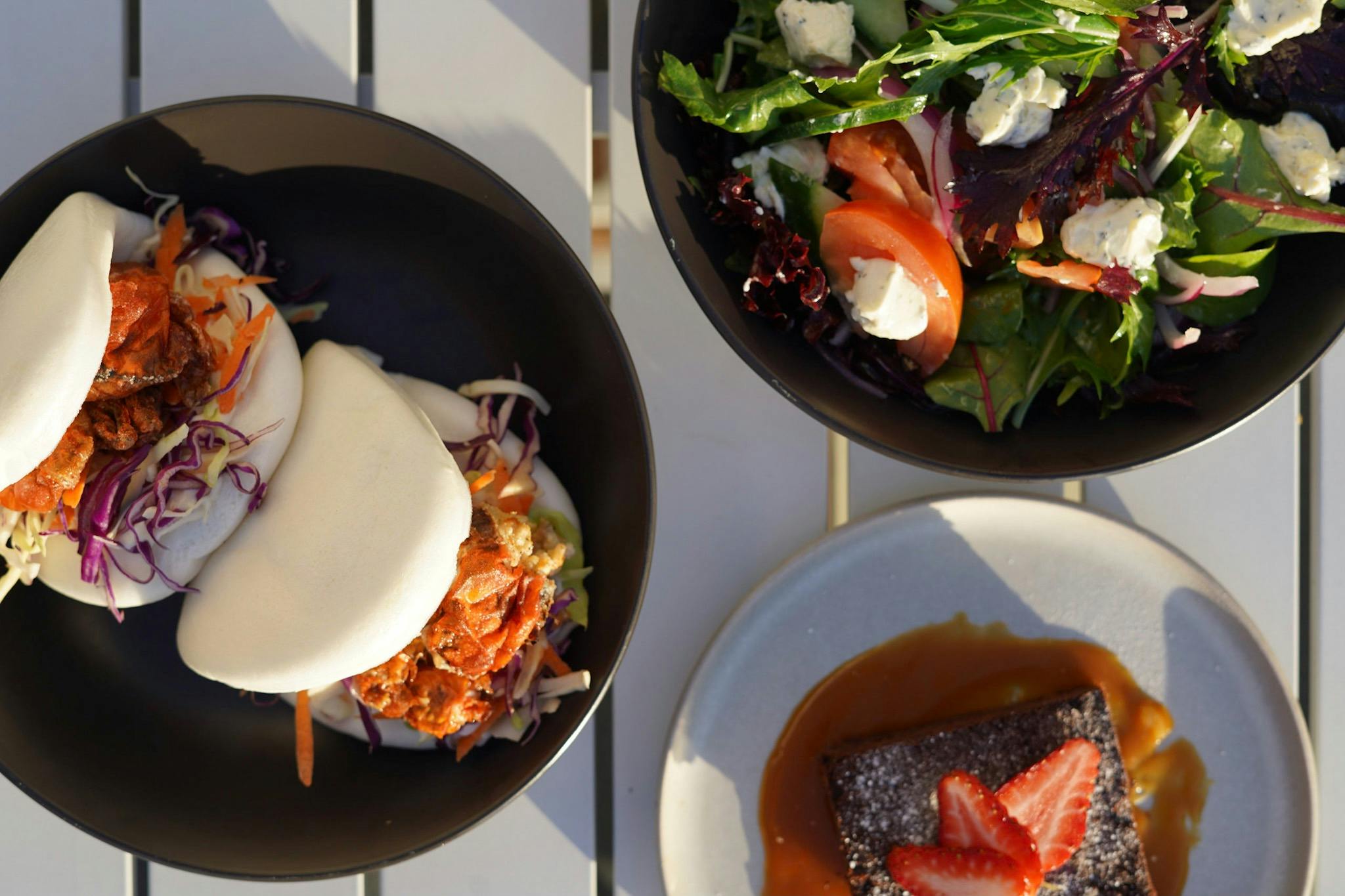Showing three plates of food with salad, bao buns and dessert options