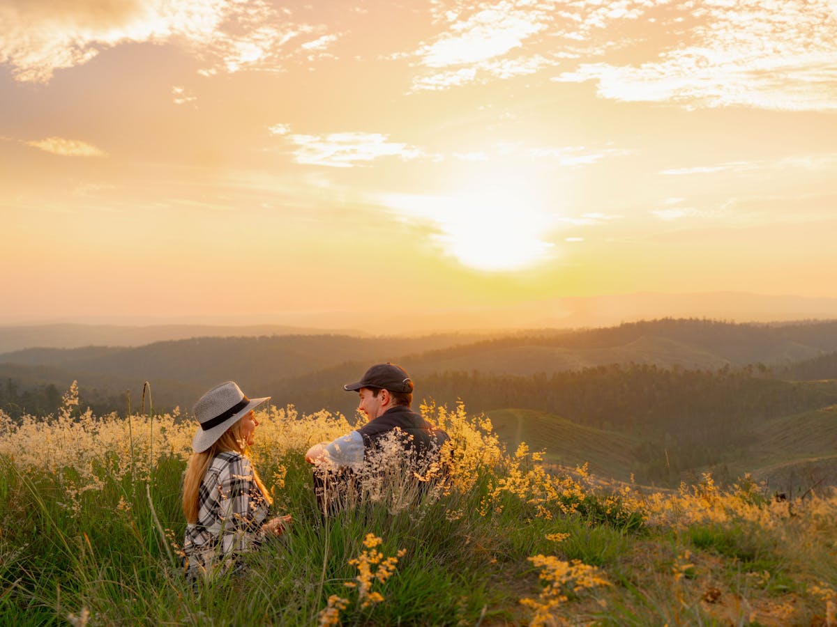 Couple sitting in grassy field watching the sunset