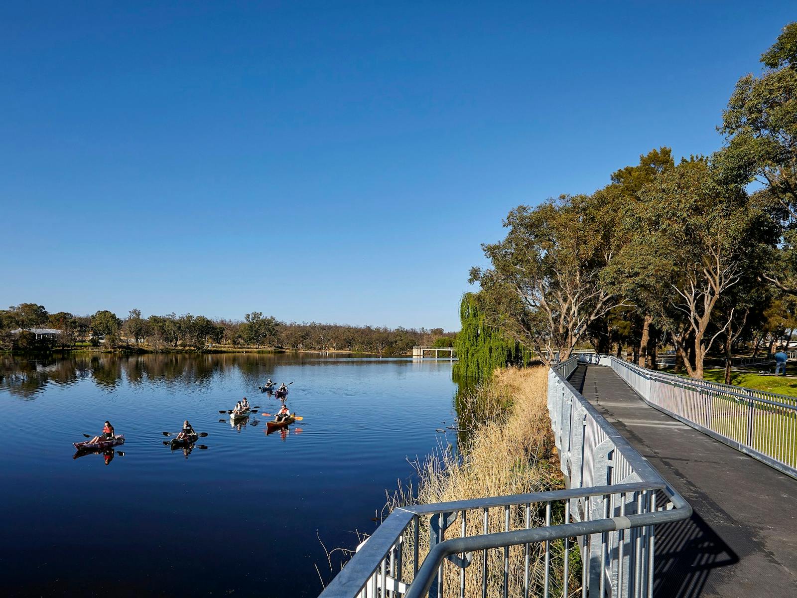 Boardwalk on right with six kayaks on Lake Inverell on left