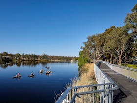 Boardwalk on right with six kayaks on Lake Inverell on left
