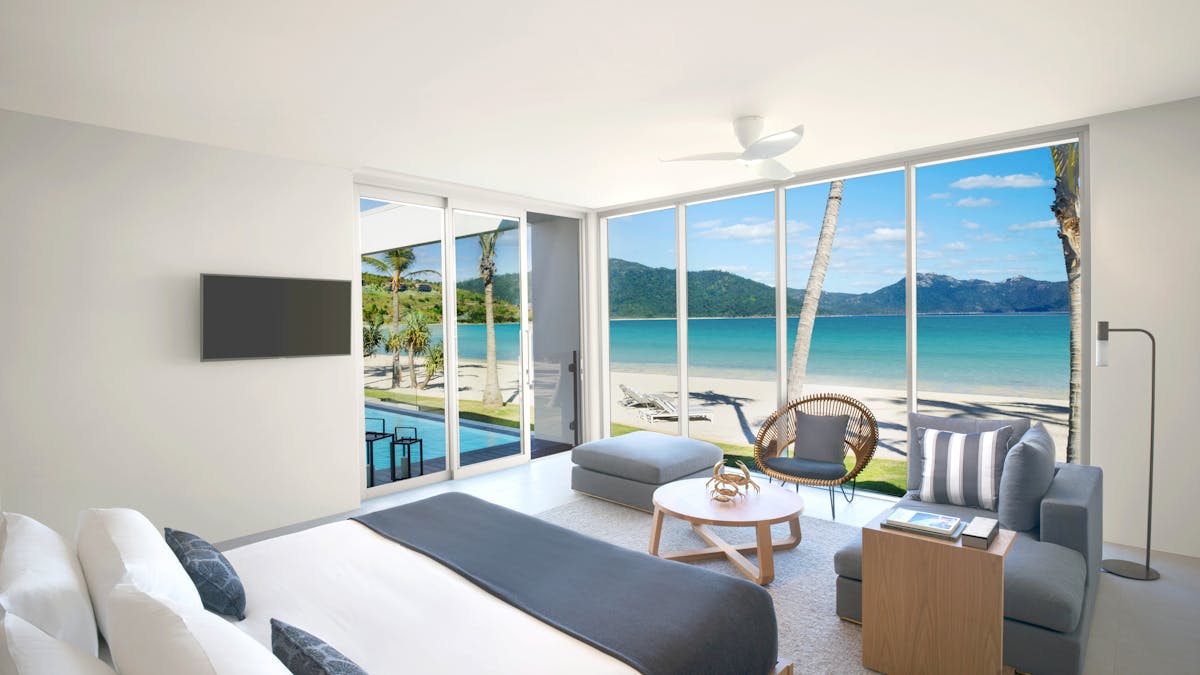 Bright, modern beachfront suite with a bed, seating area, large windows, pool, and ocean views.