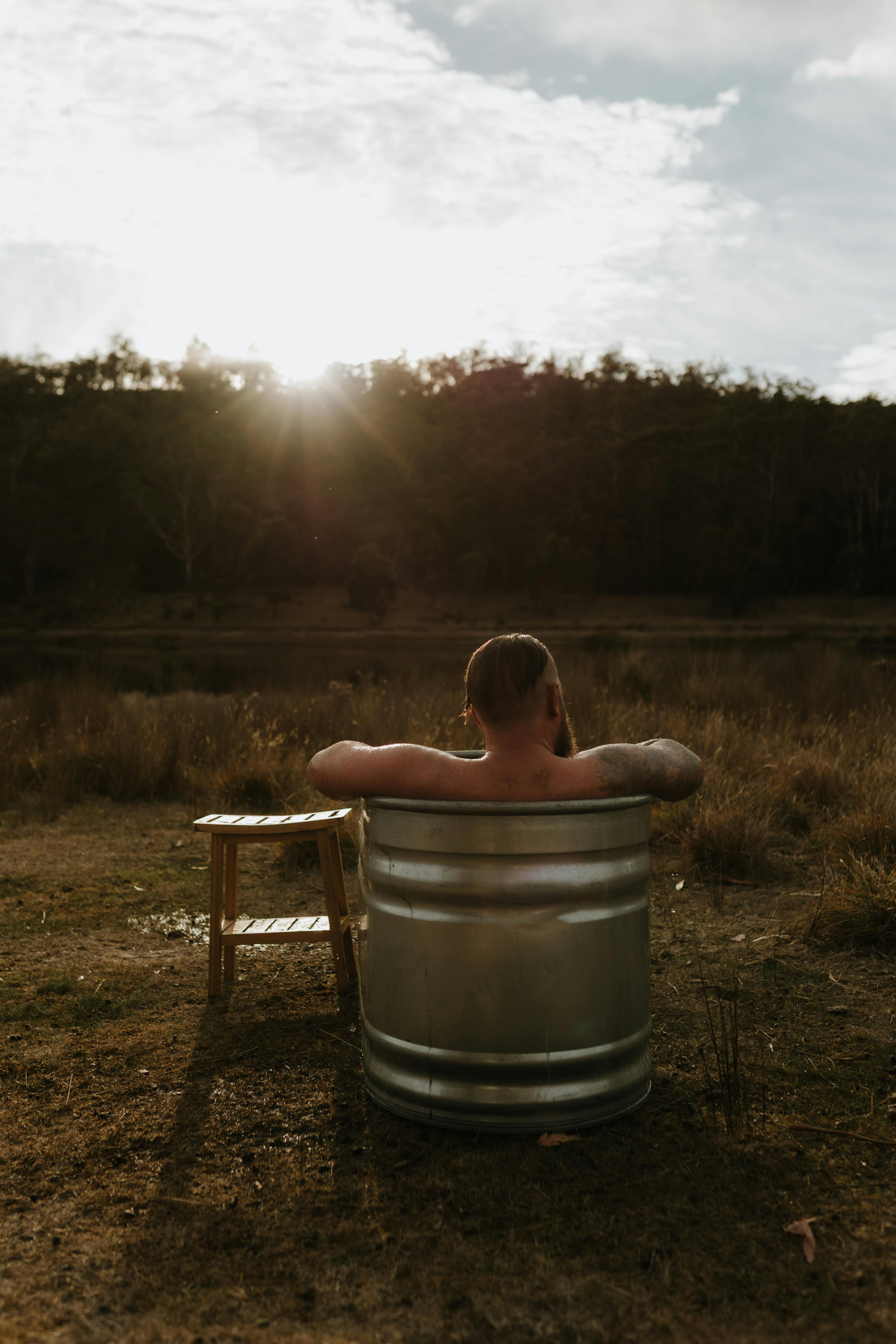Person relaxing in an outdoor ice bath overlooking a river and native bushland.