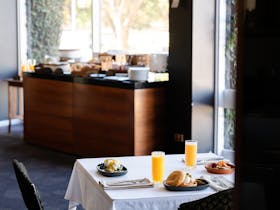A table in the restaurant set with orange juice and breakfast meals. In the background is a buffet
