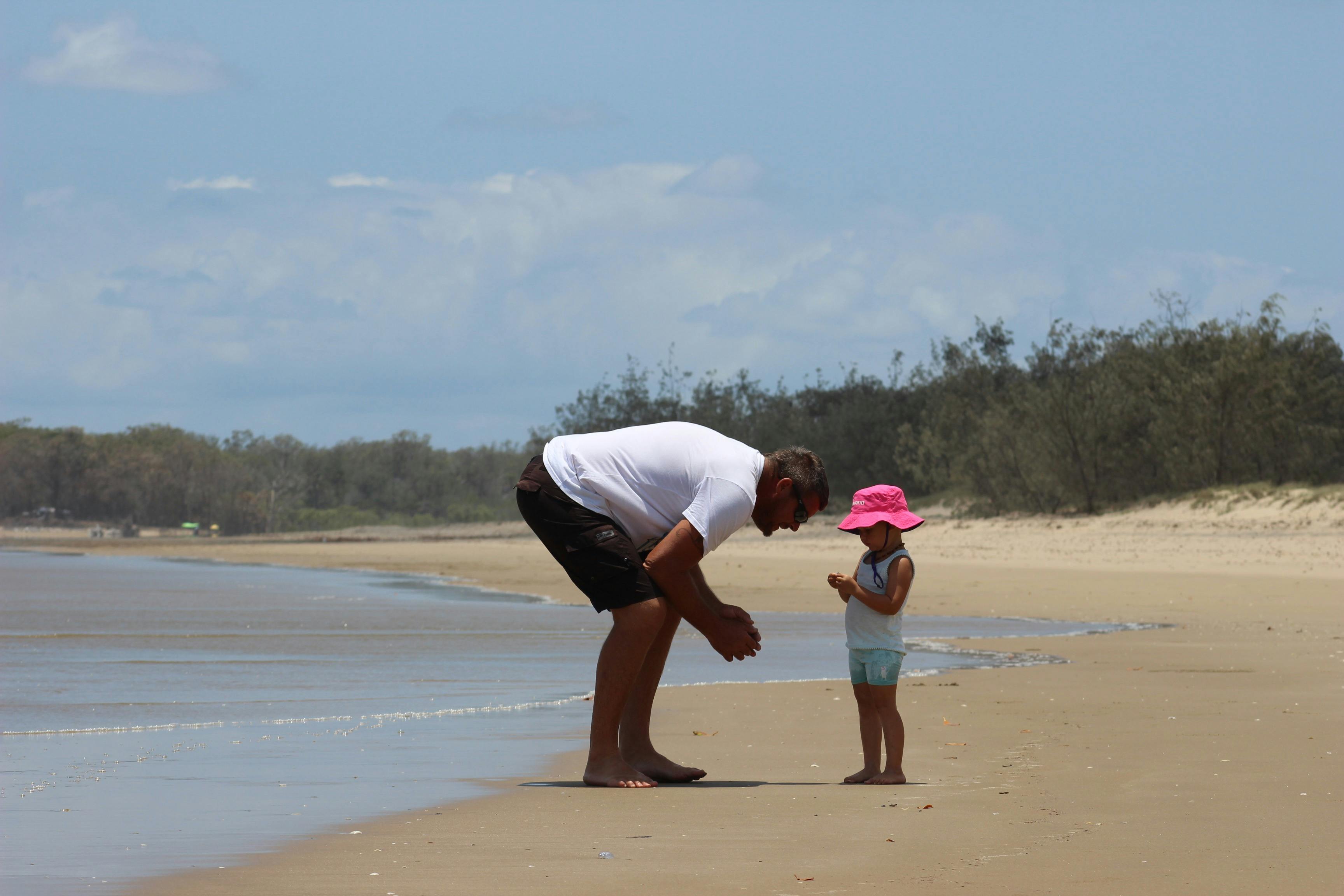 Father and young daughter on the beach combing for sea shells.