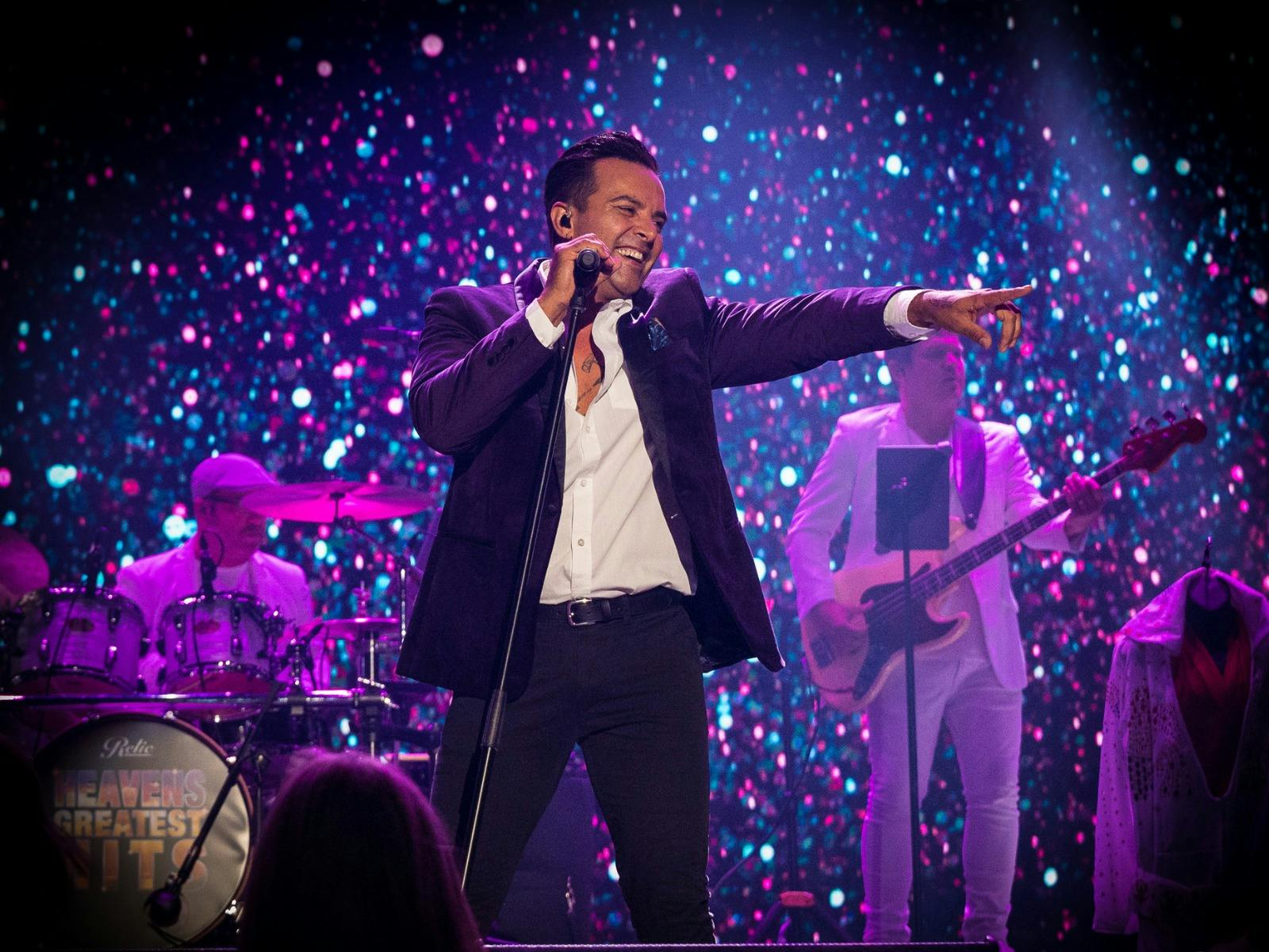Jason Singh smiling and pointing on stage with purple sparkly background