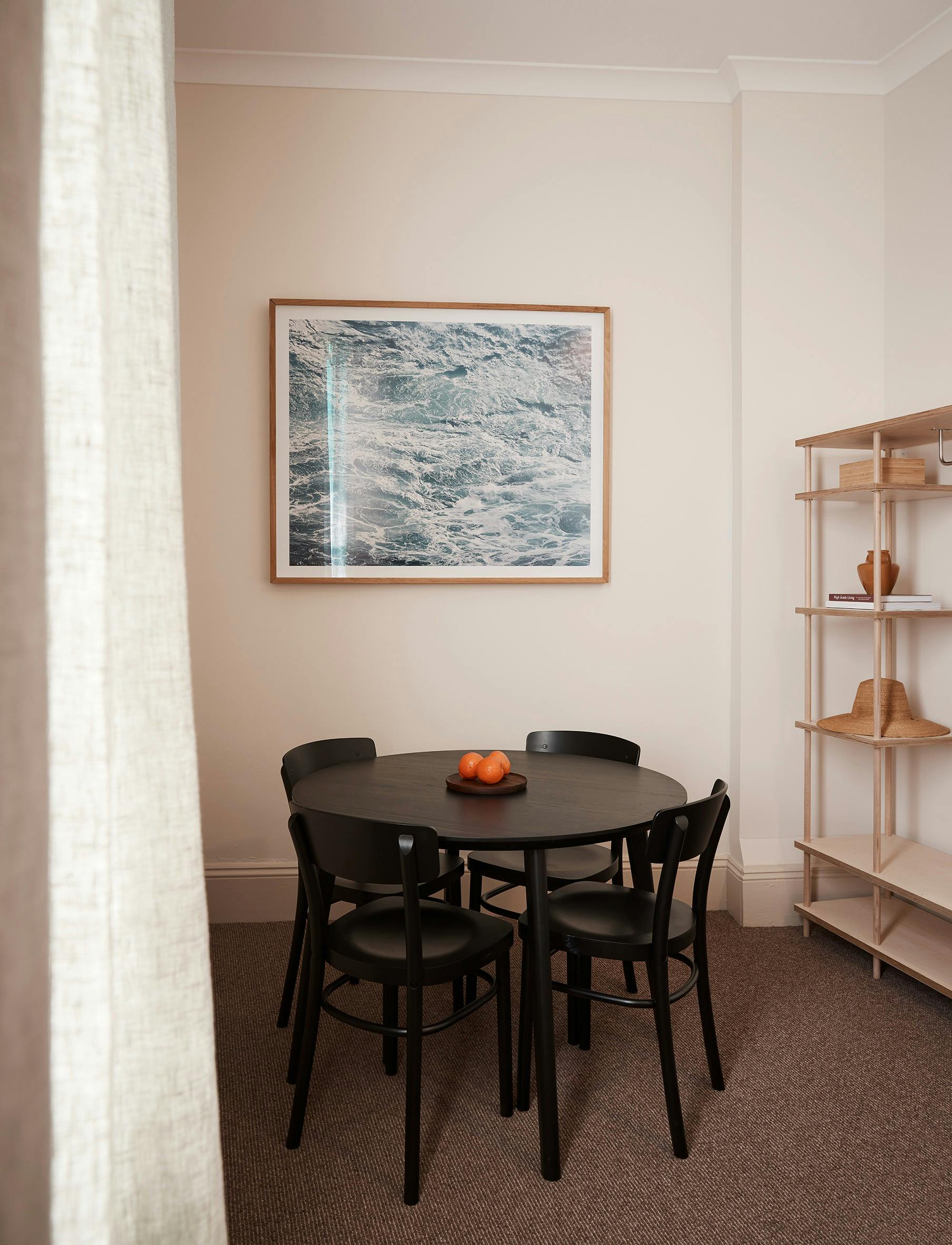 Cozy dining nook with round black table, four chairs, and ocean-themed artwork