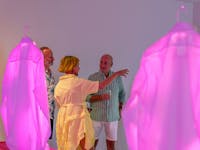Installation of dress shirts with projected images illuminating them in bight pink. 3 people behind.