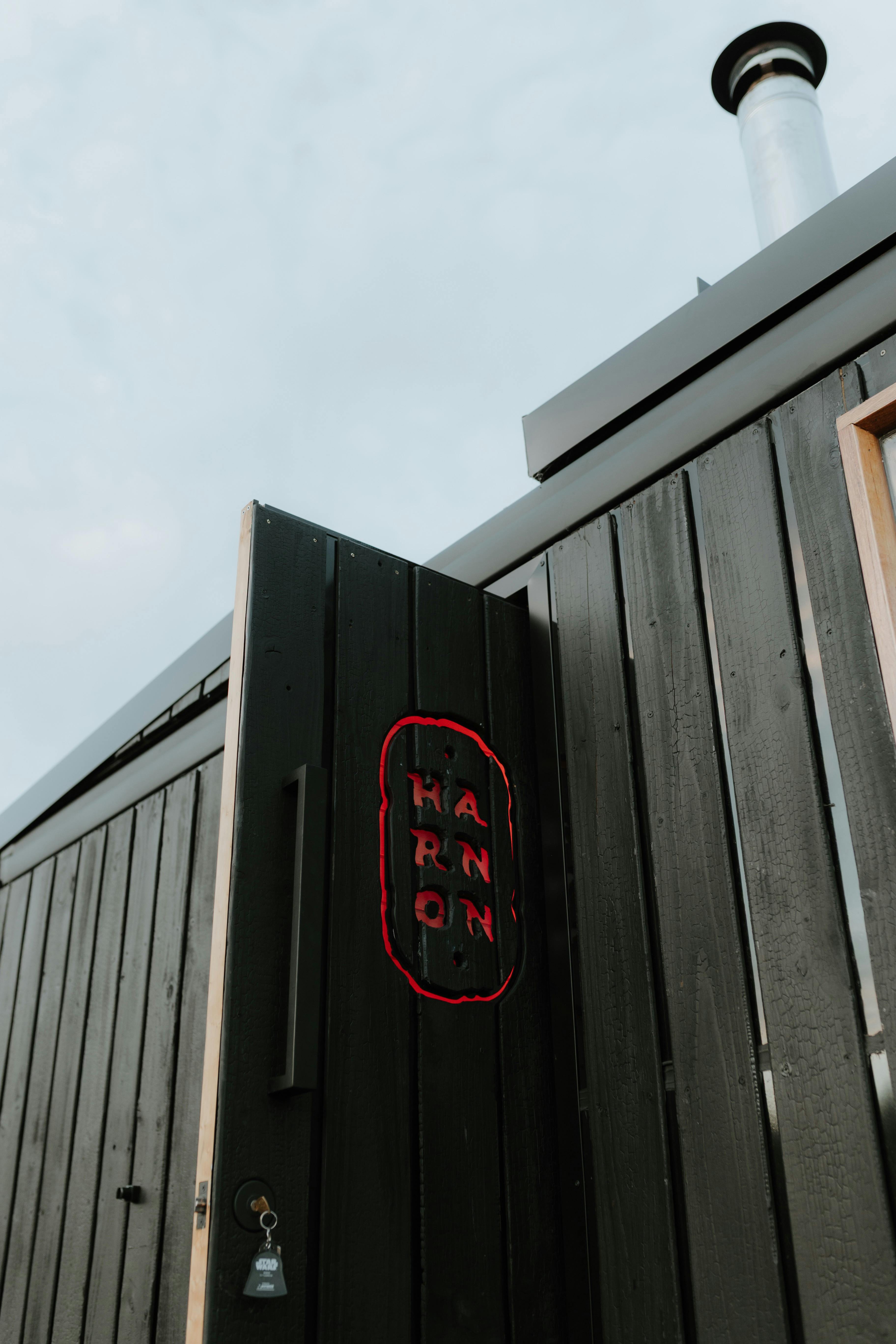 Black timber sauna exterior with Harnon signage and wood-fired chimney.