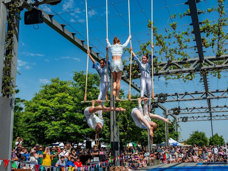5 aerialists in silver costumes perform on a triple trapeze.