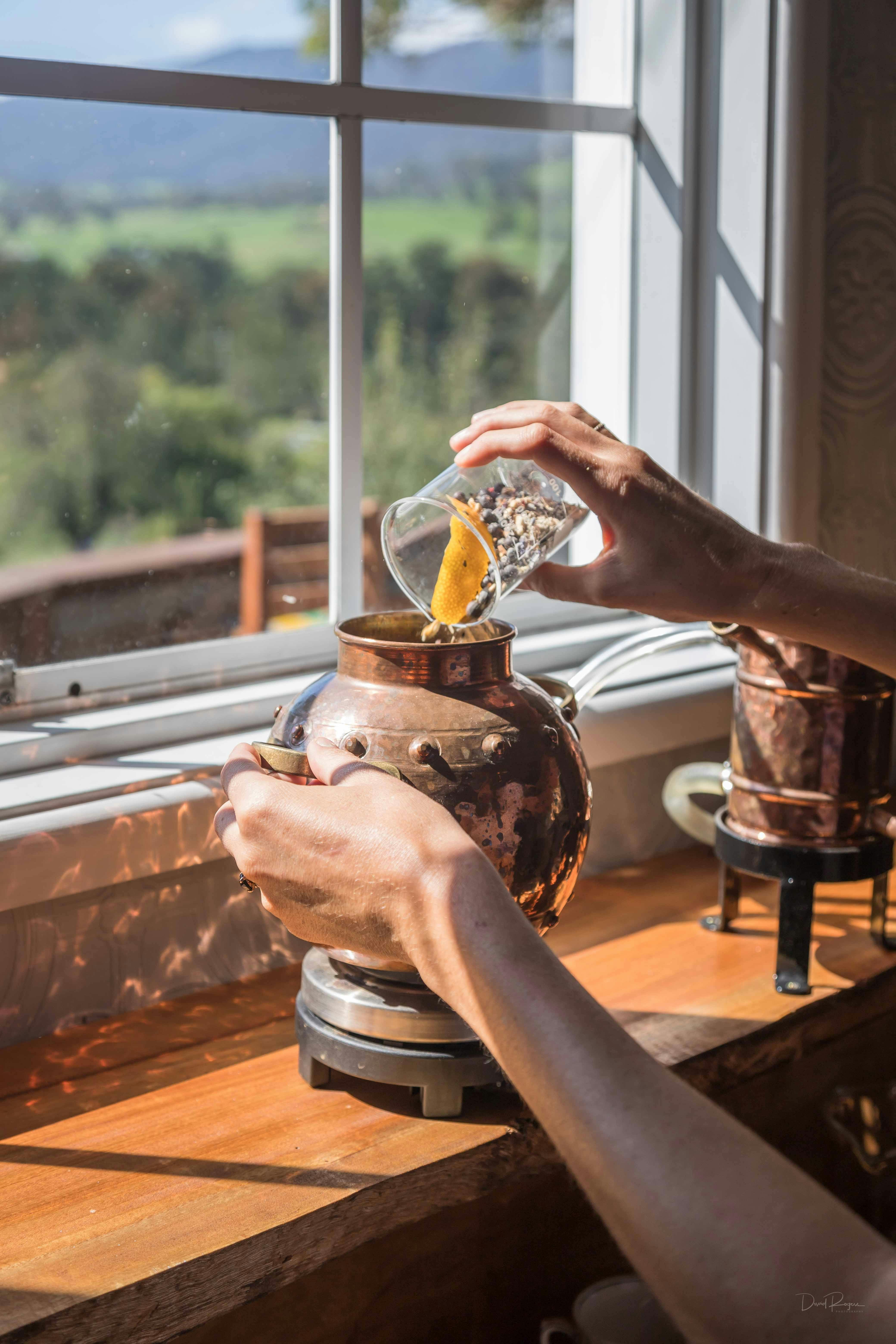 Close up of botanicals being put into a small copper still