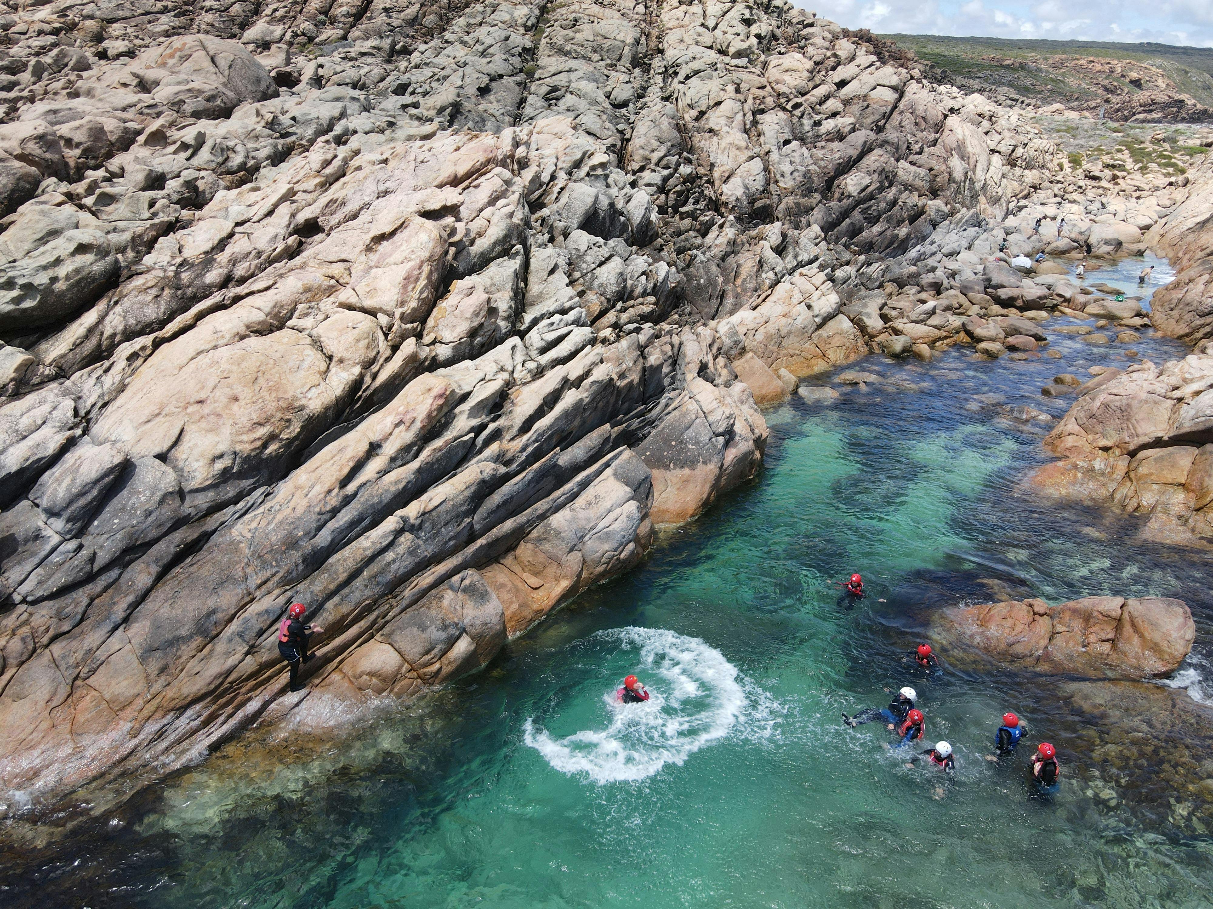 Distant view of hiking group in calm clear pool of water surrounded by large rock cliffs