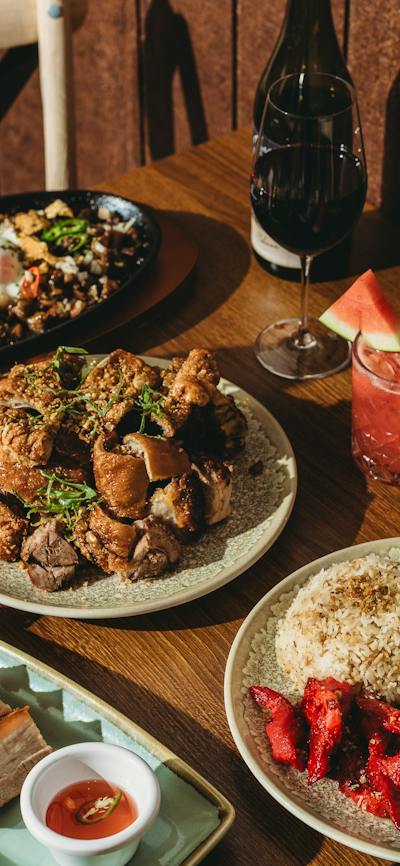 A wooden dining table filled with Filipino dishes including crispy pork belly, fried rice with eggs,