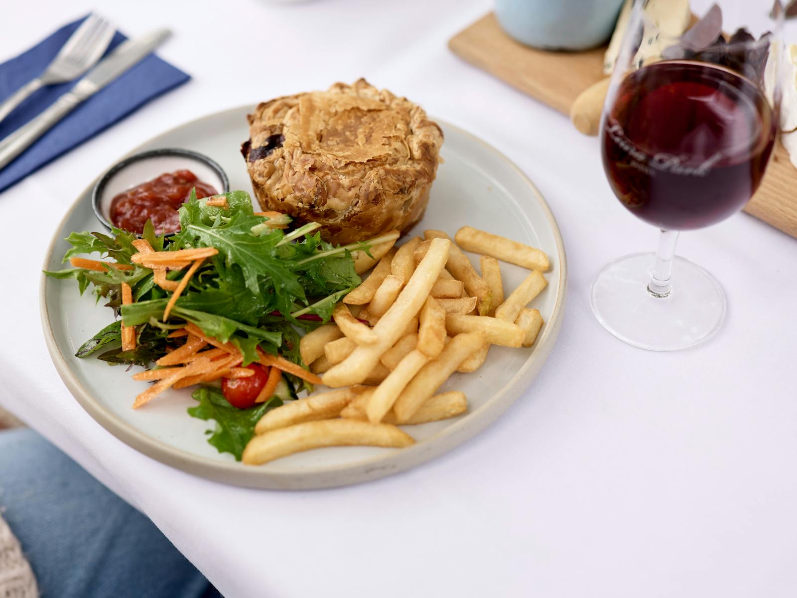 White tablecloth, a plate with a pie, chips and salad, and a glass of red wine