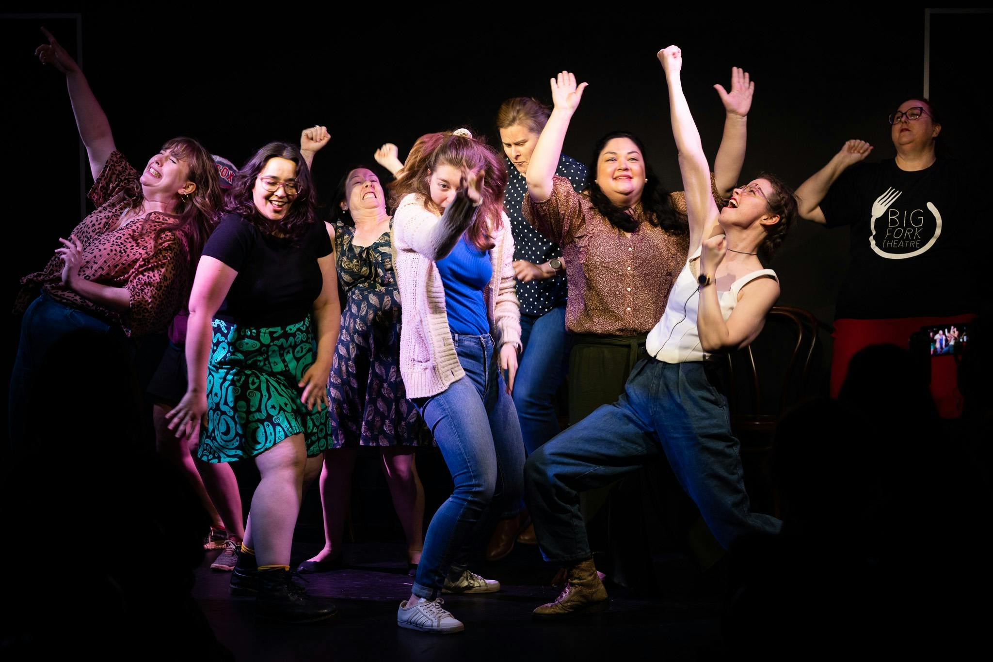 Several women pulling poses and dancing on stage while laughing