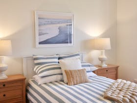 Bedroom with a queen bed, bedside tables, lamps and framed coastal artwork.