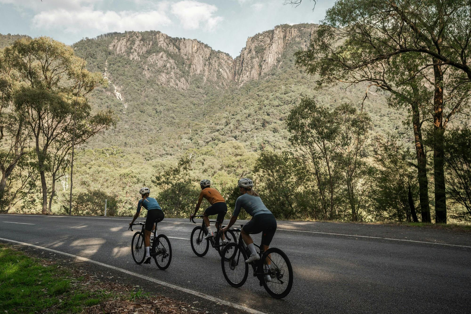 Three cyclists riding past mountain views on the Mt Buffalo 7 Peaks Challenge route.