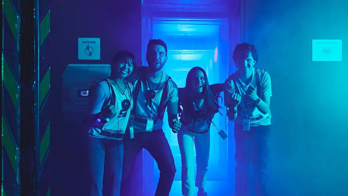 Four adults in Saboteurs vests grin together in a blue-lit corridor after a game.