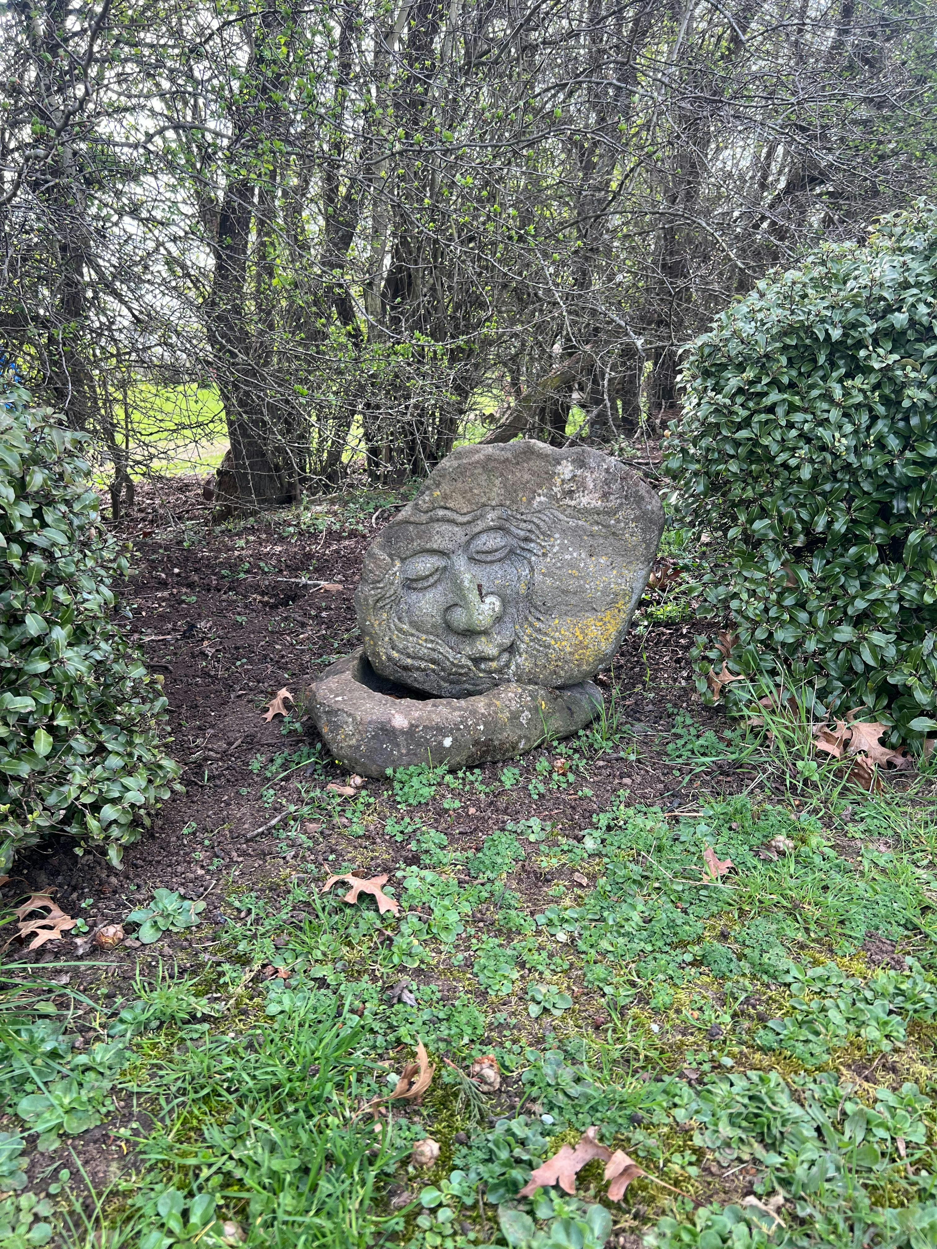 a stone carving in the garden bushes