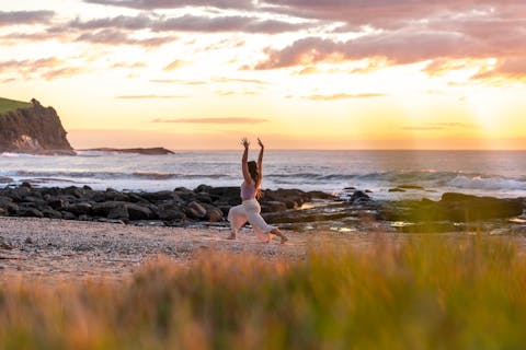 A young woman practices yoga on the beach at sunrise
