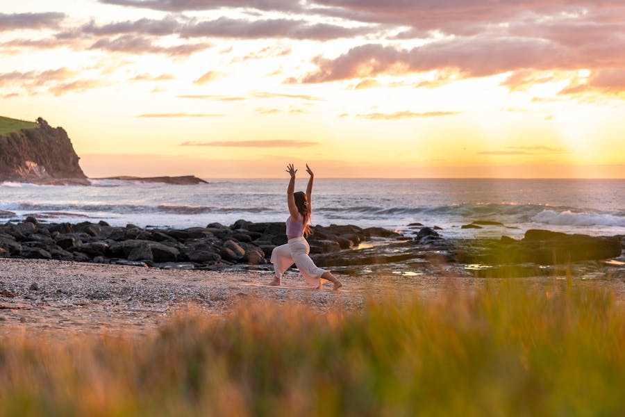 A young woman practices yoga on the beach at sunrise