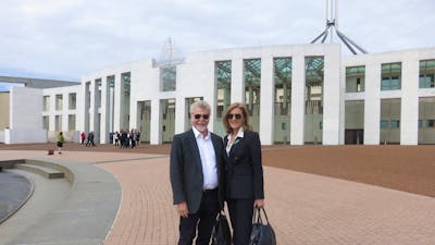 A man and a woman standing in front of the Parliament House in Canberra