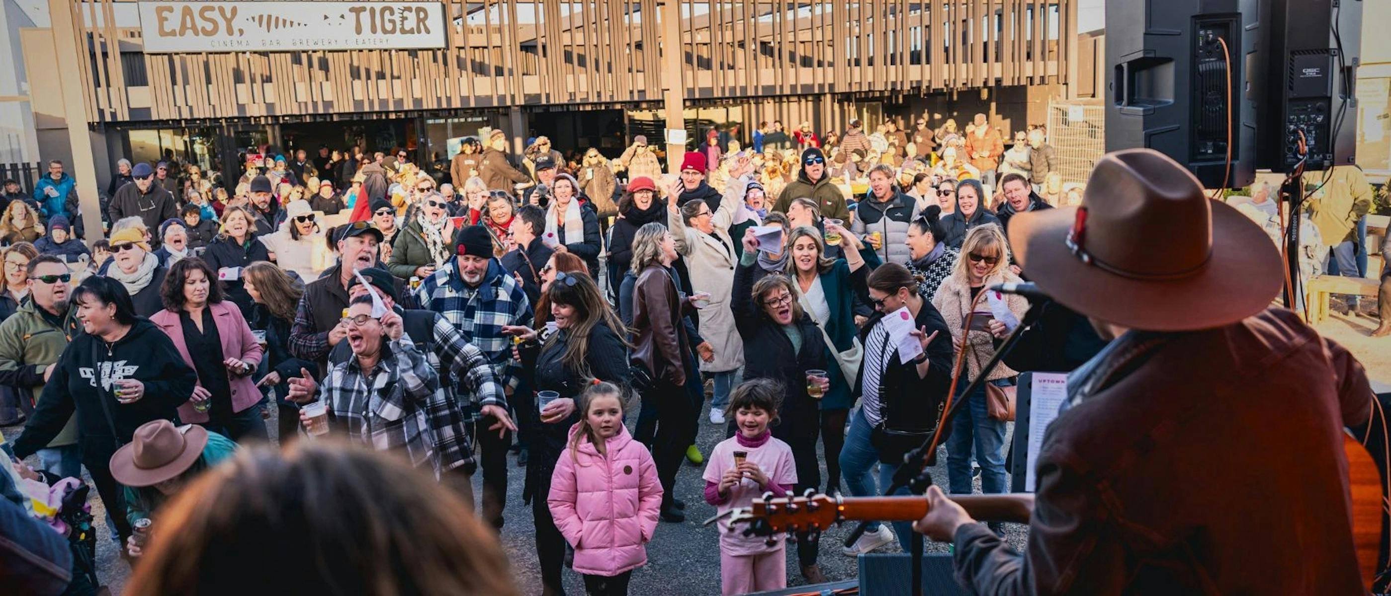 An audience of all ages dancing outdoors in front of a stage