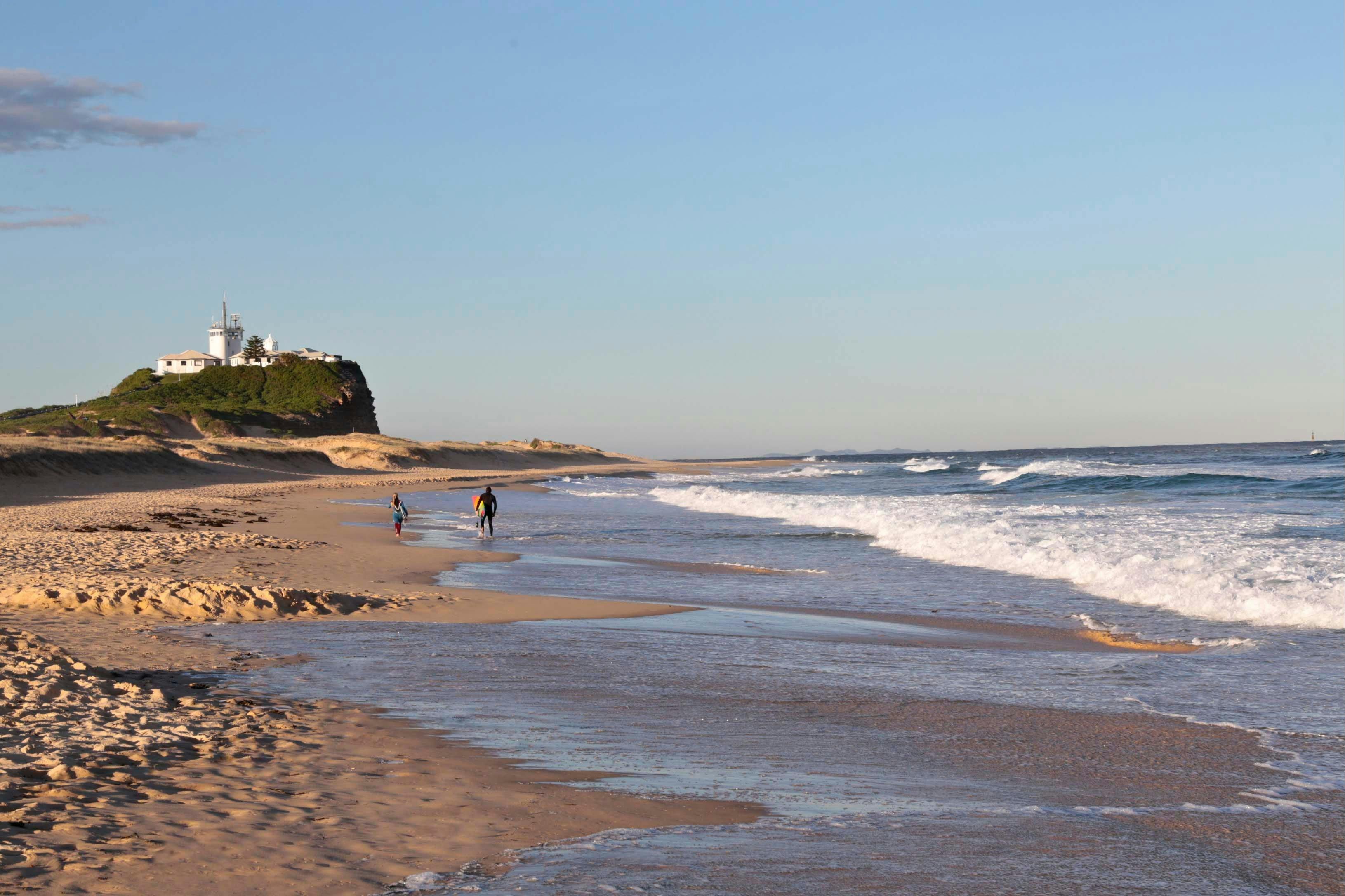 Surfers walking along Nobbys Beach towards Nobbys Lighthouse