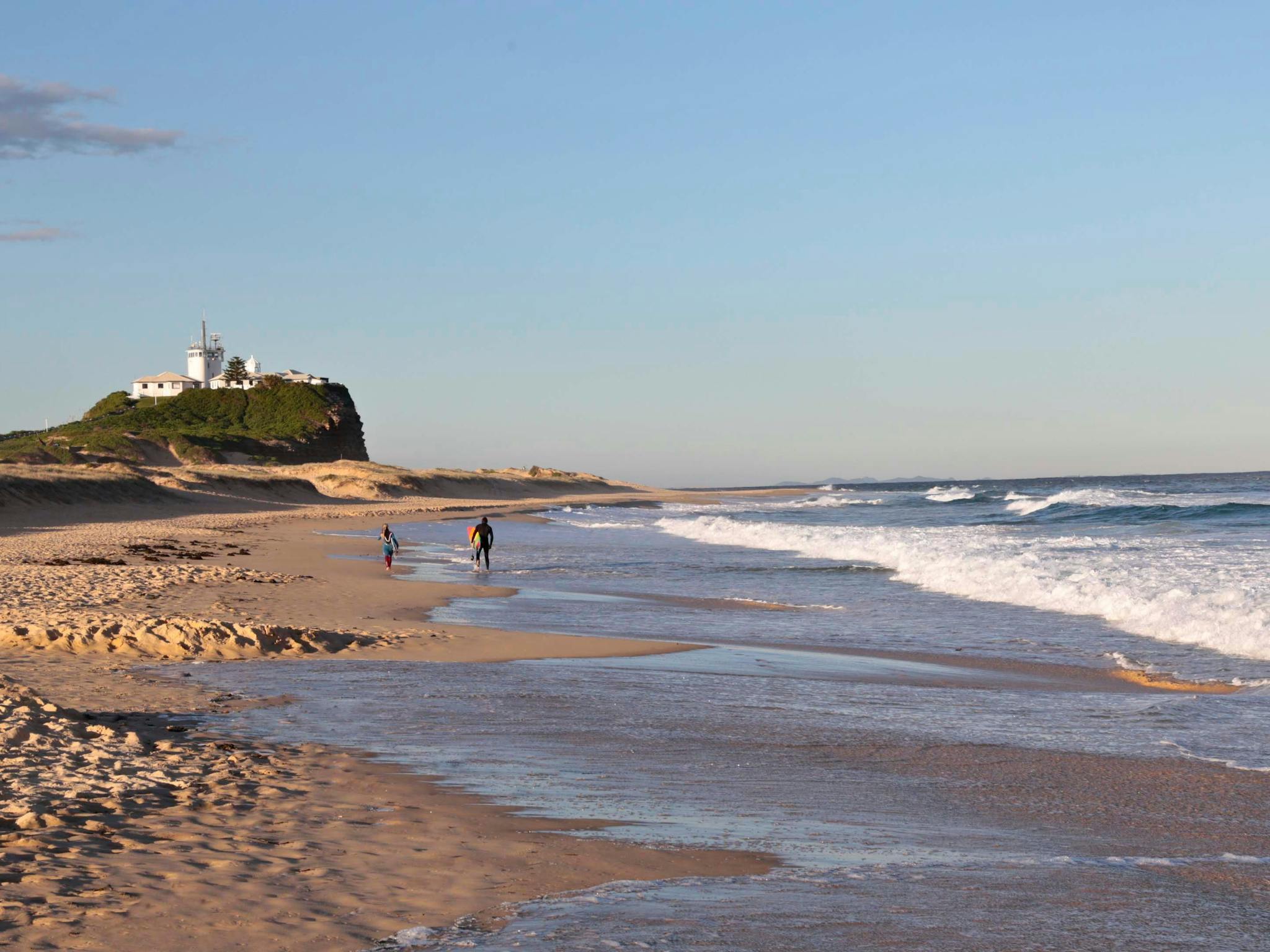 Surfers walking along Nobbys Beach towards Nobbys Lighthouse