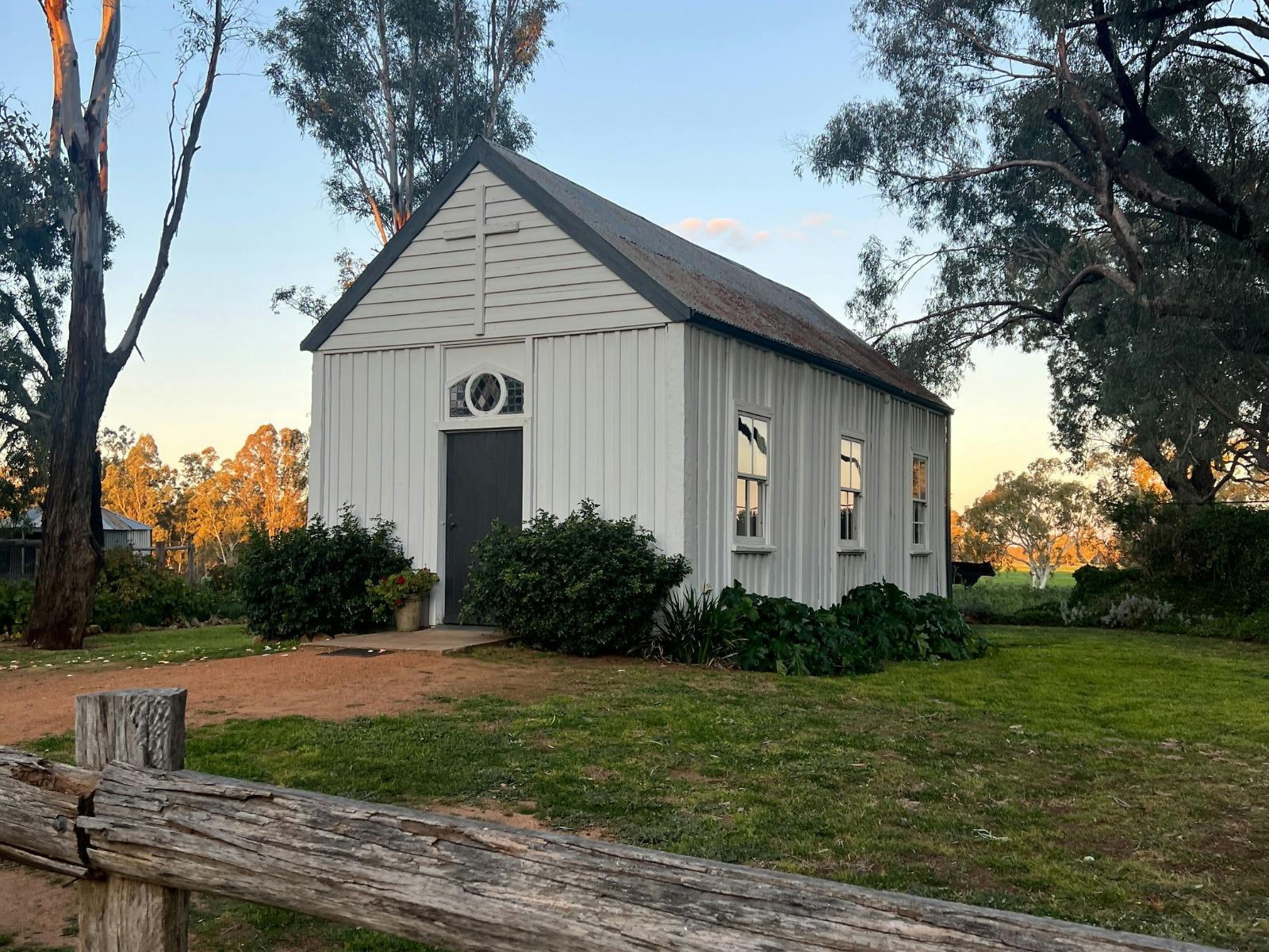 Old white timber church sits under old trees