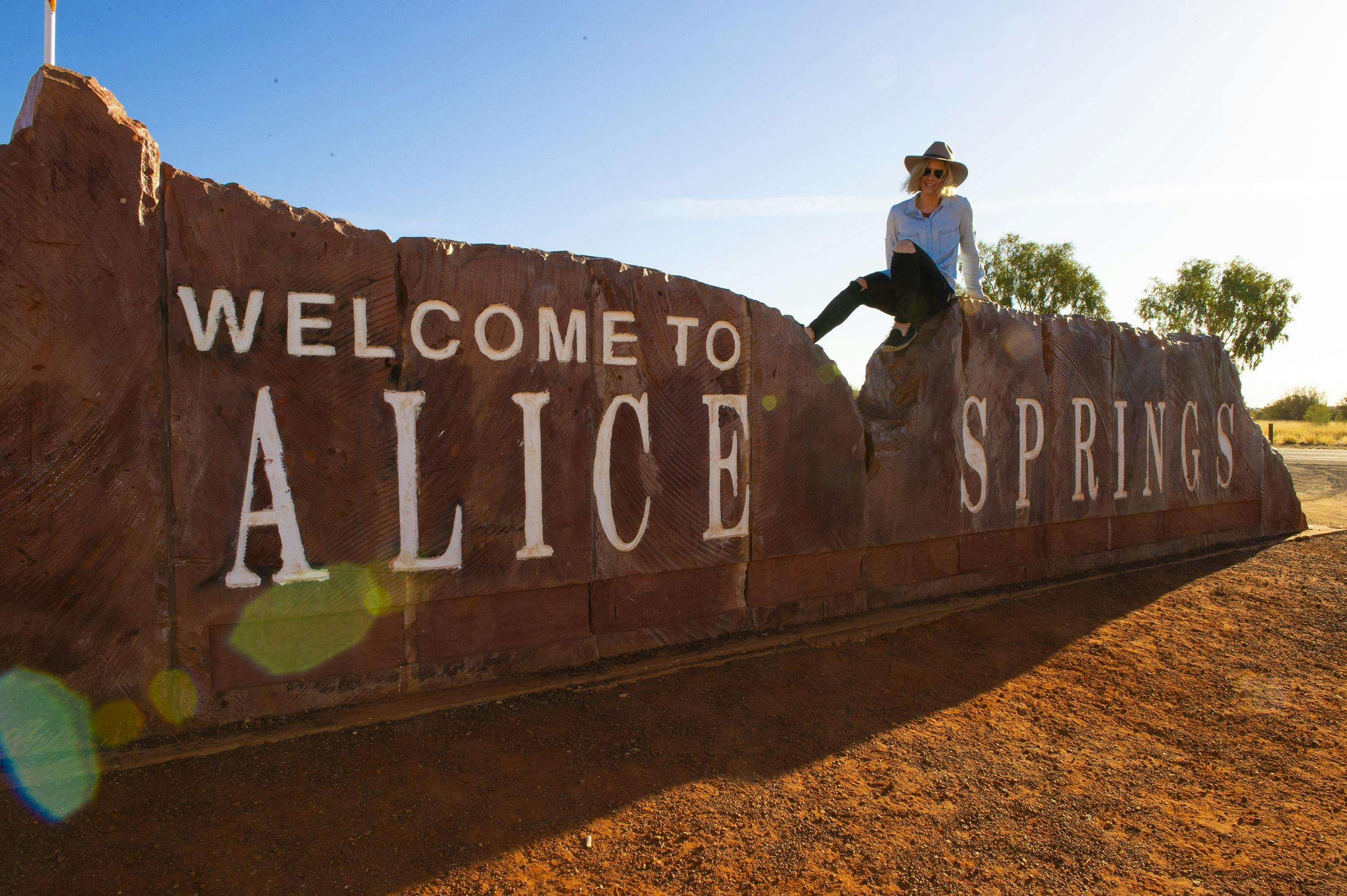 Woman sitting on the Welcome to Alice Springs sign