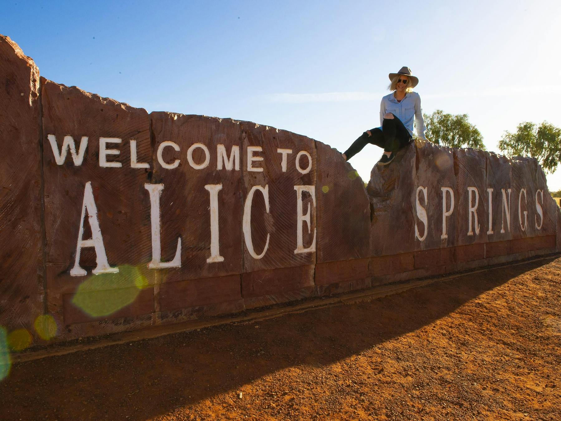Woman sitting on the Welcome to Alice Springs sign