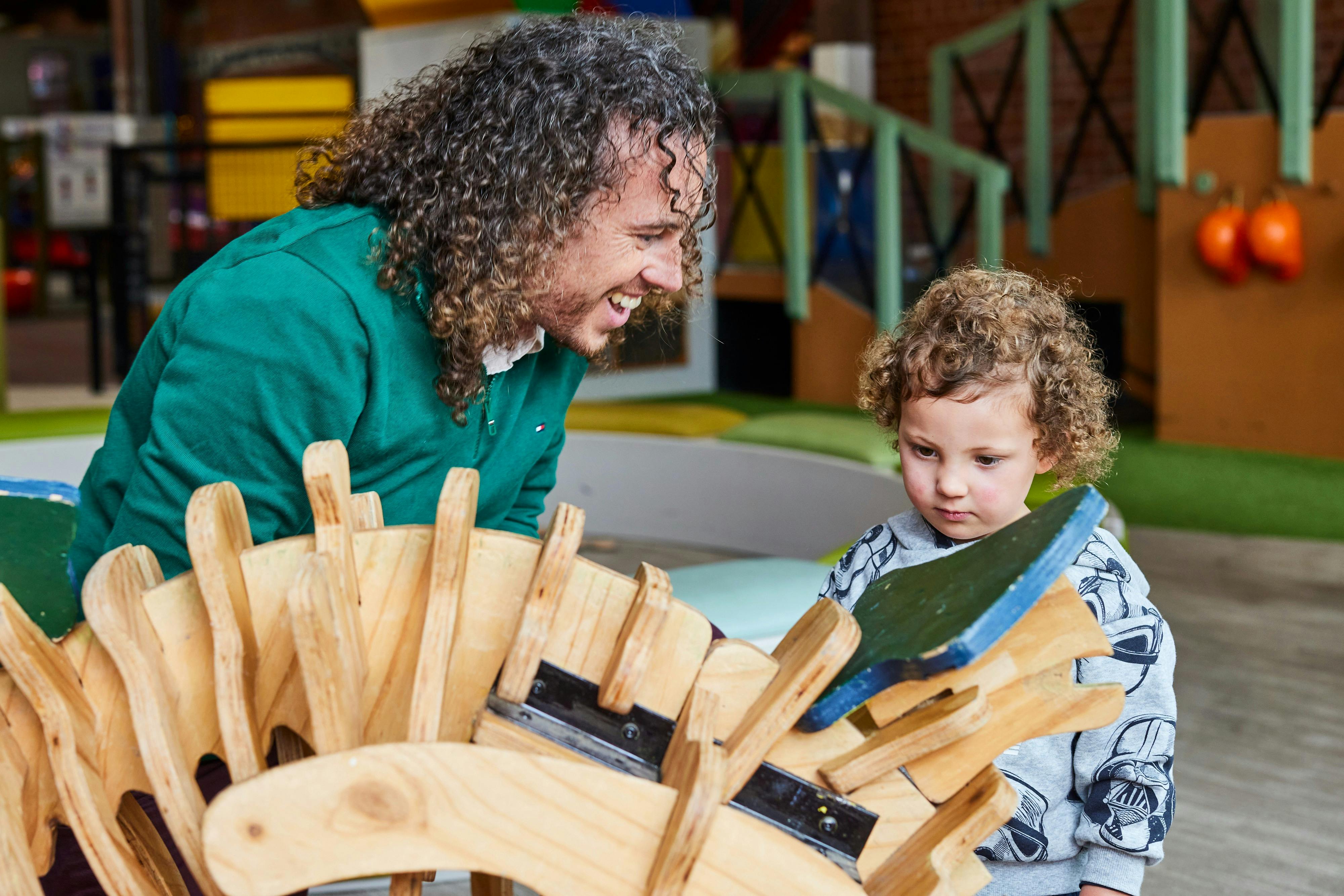 Father helping toddler build a wooden dinosaur in the under 5's playspace