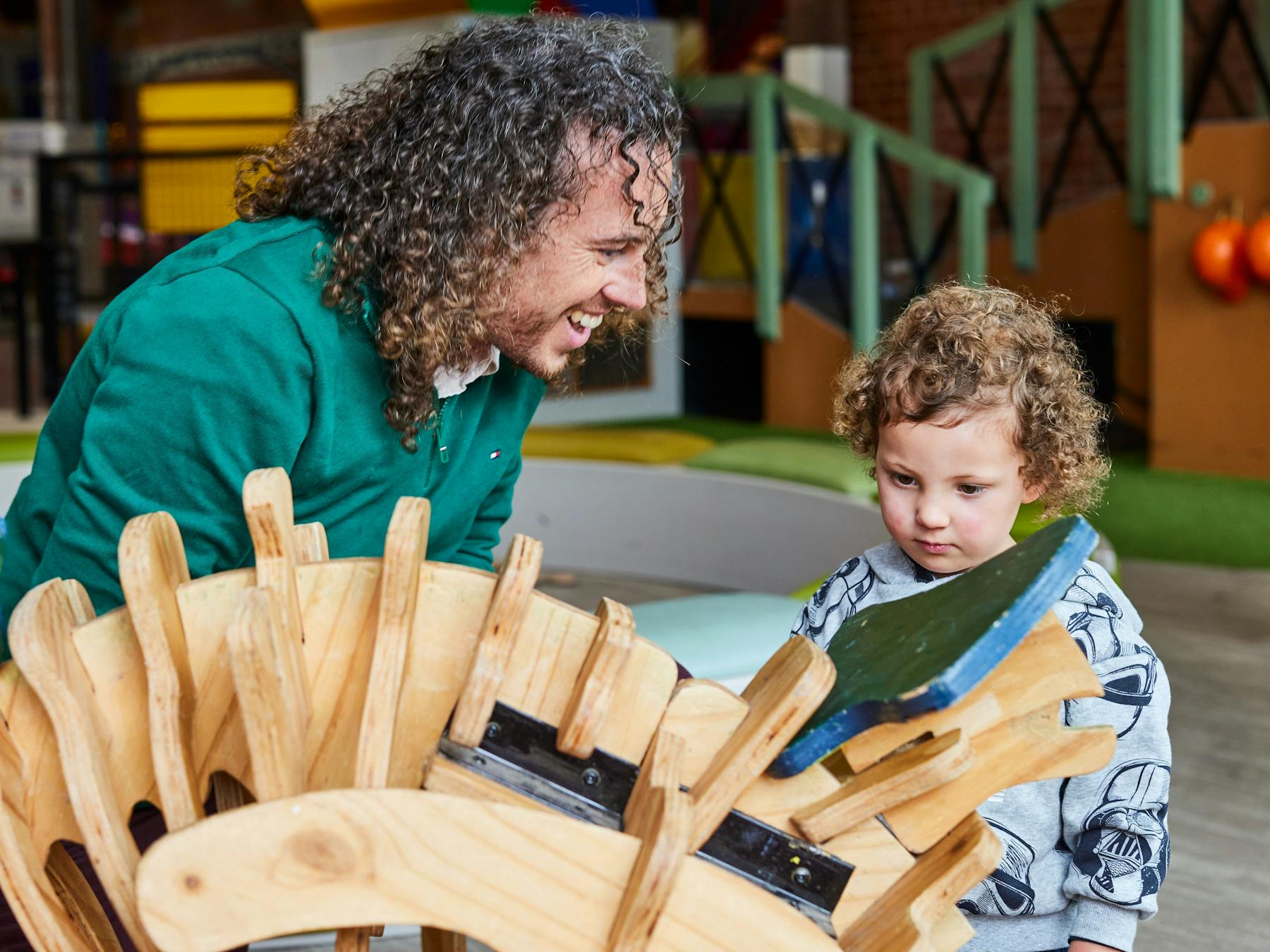 Father helping toddler build a wooden dinosaur in the under 5's playspace