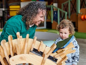 Father helping toddler build a wooden dinosaur in the under 5's playspace