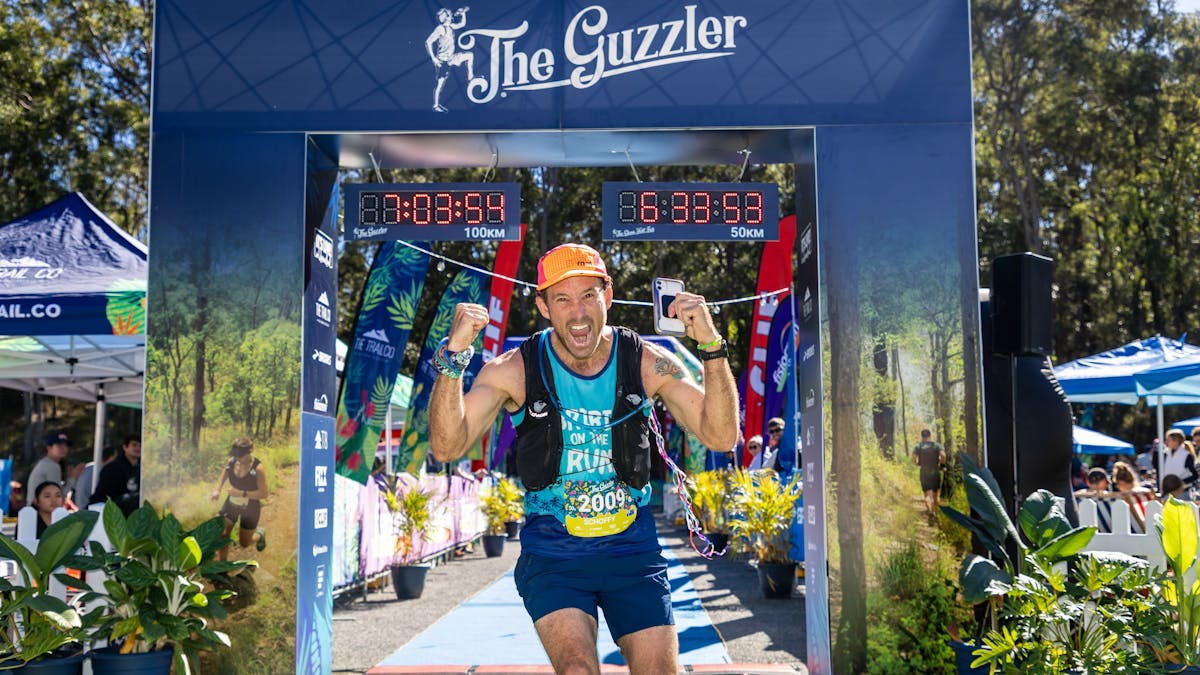 An excited runner smiles at the camera after crossing underneath The Guzzler finish arch