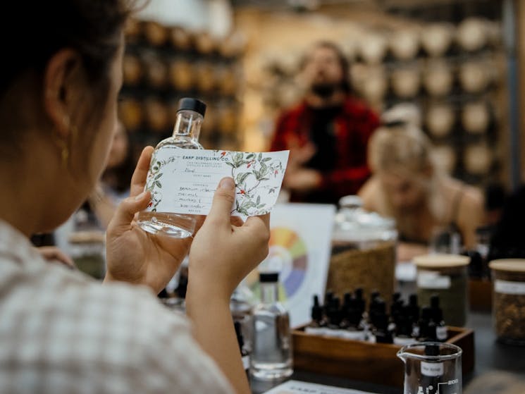 A woman wraps a hand written label around her bottle of blended gin