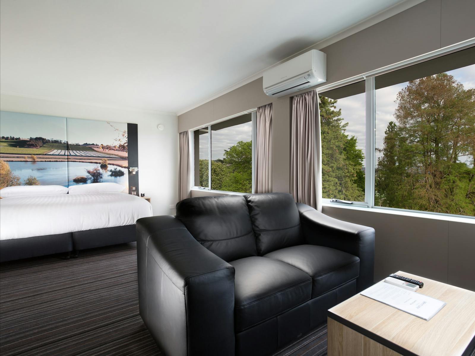 Guest accommodation room, with lounge suite and king bed, two large windows with sky/trees view.