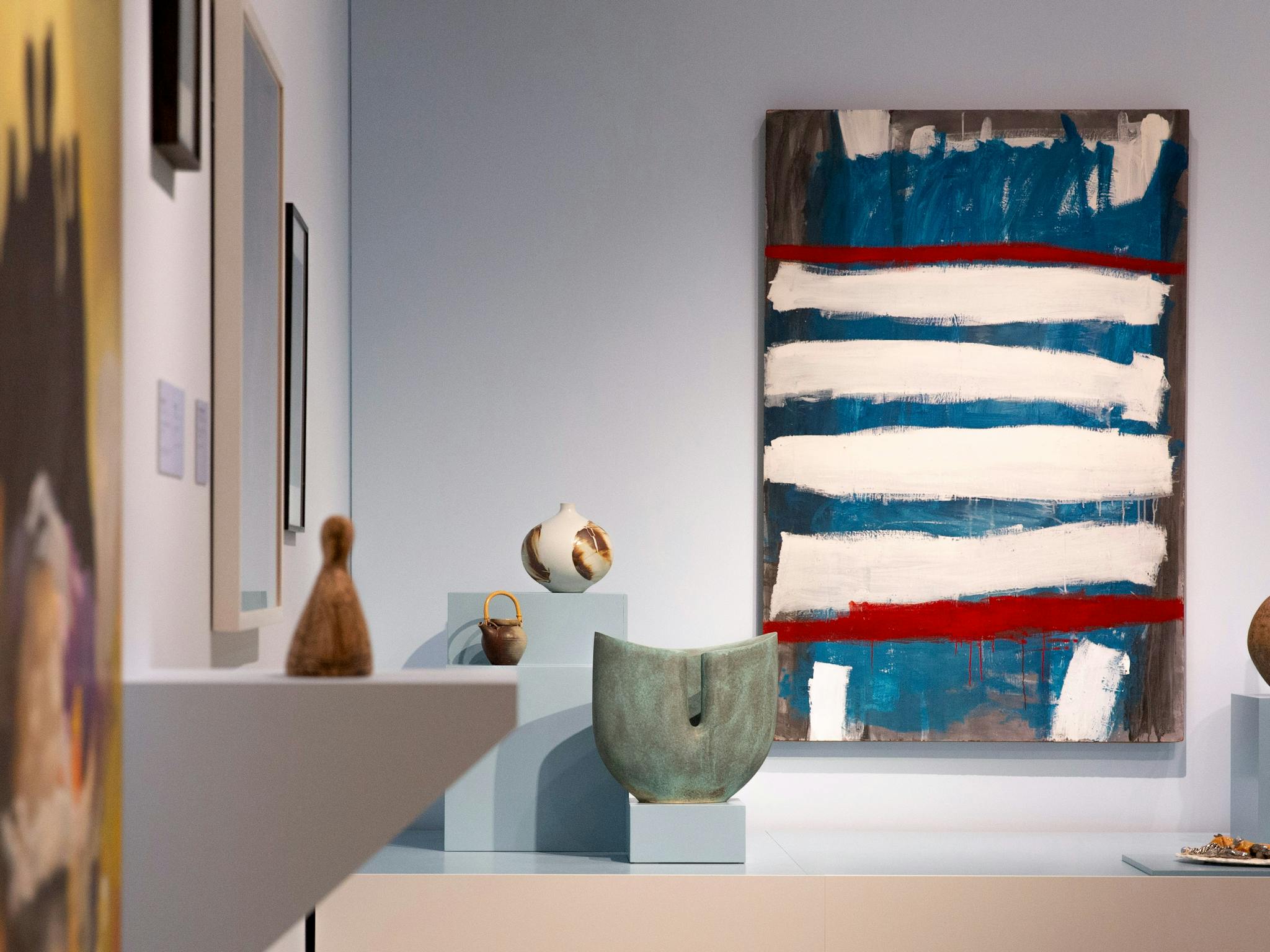 A view of a gallery with paintings on its walls, and ceramics on plints of varying heights