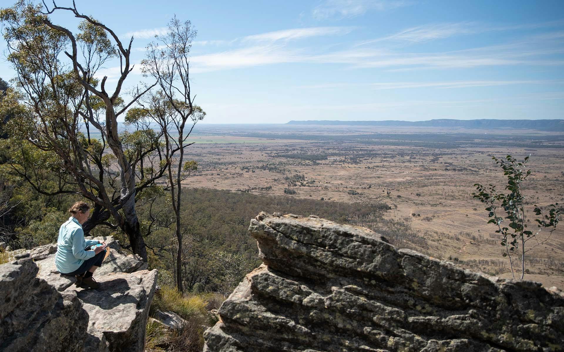 A woman sitting on a rock at the edge of the bush, overlooking Carnarvon Gorge