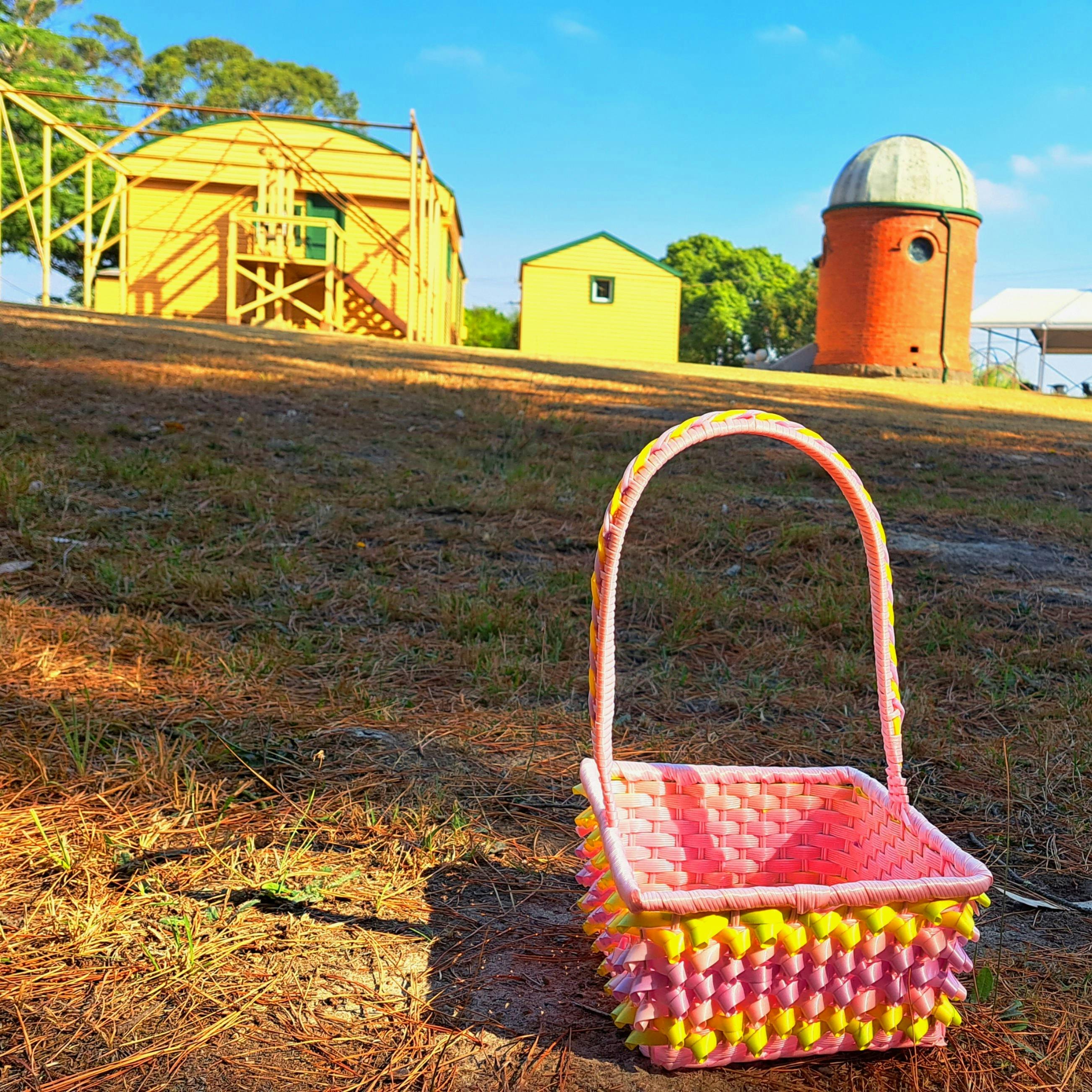 pink and yellow basket on ground in front of 2 yellow buildings and one observatory dome