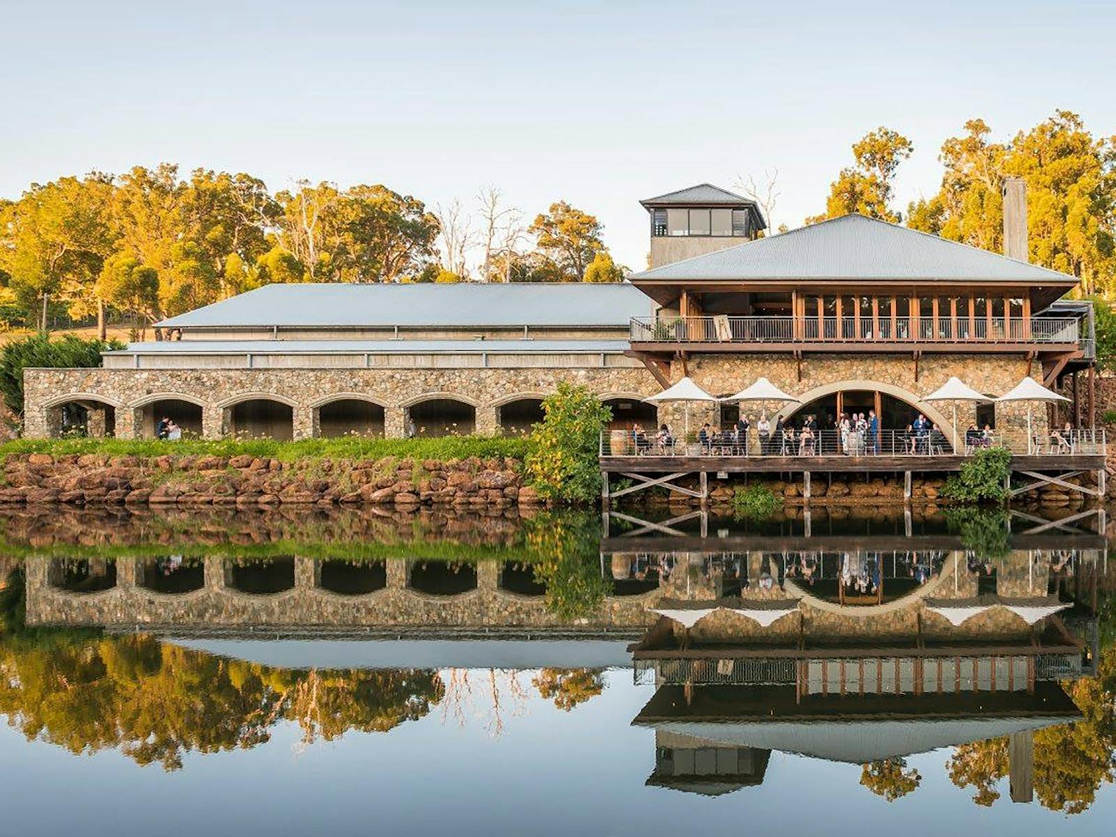 A large building with stone and wood elements is reflected in a calm body of water situated infront