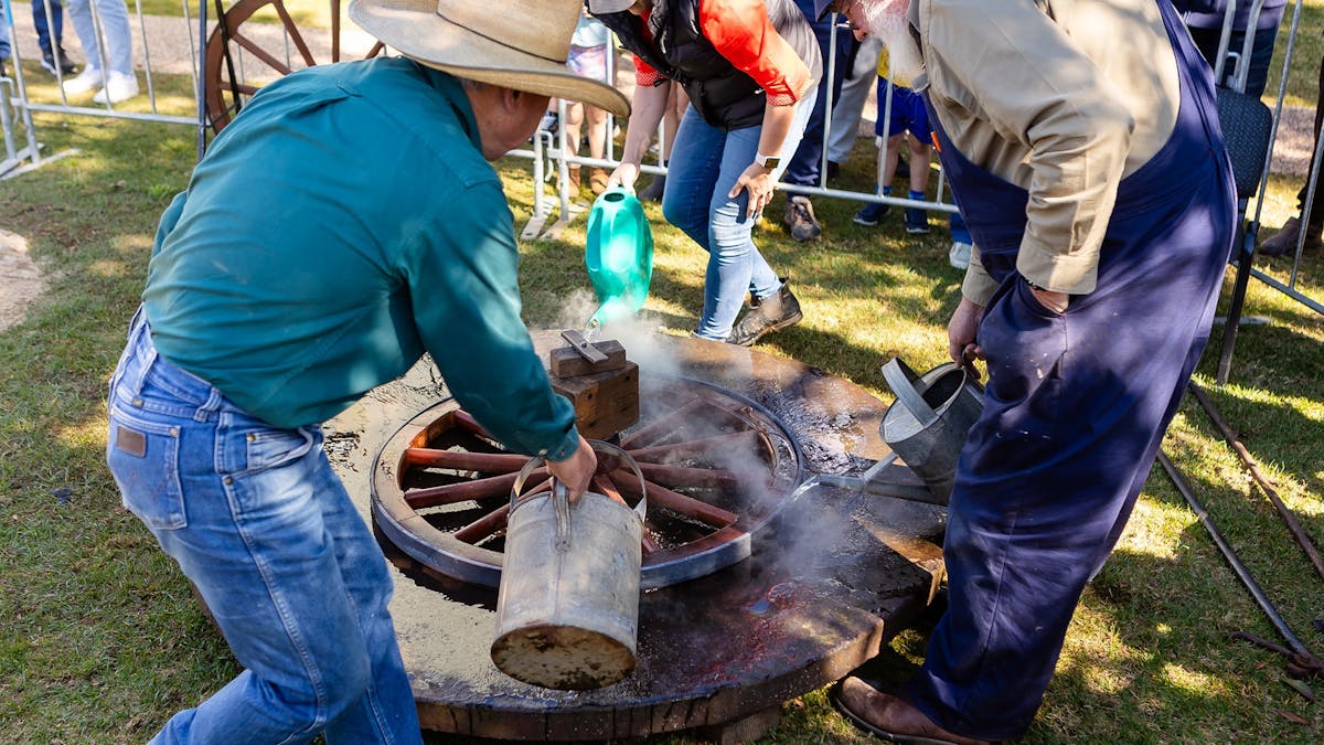 3 craftsmen cooling a heated metal wheel rim to attach it to wooden wagon wheel. 3 craftsmen cooling a heated metal wheel rim to attach it to wooden wagon wheel.